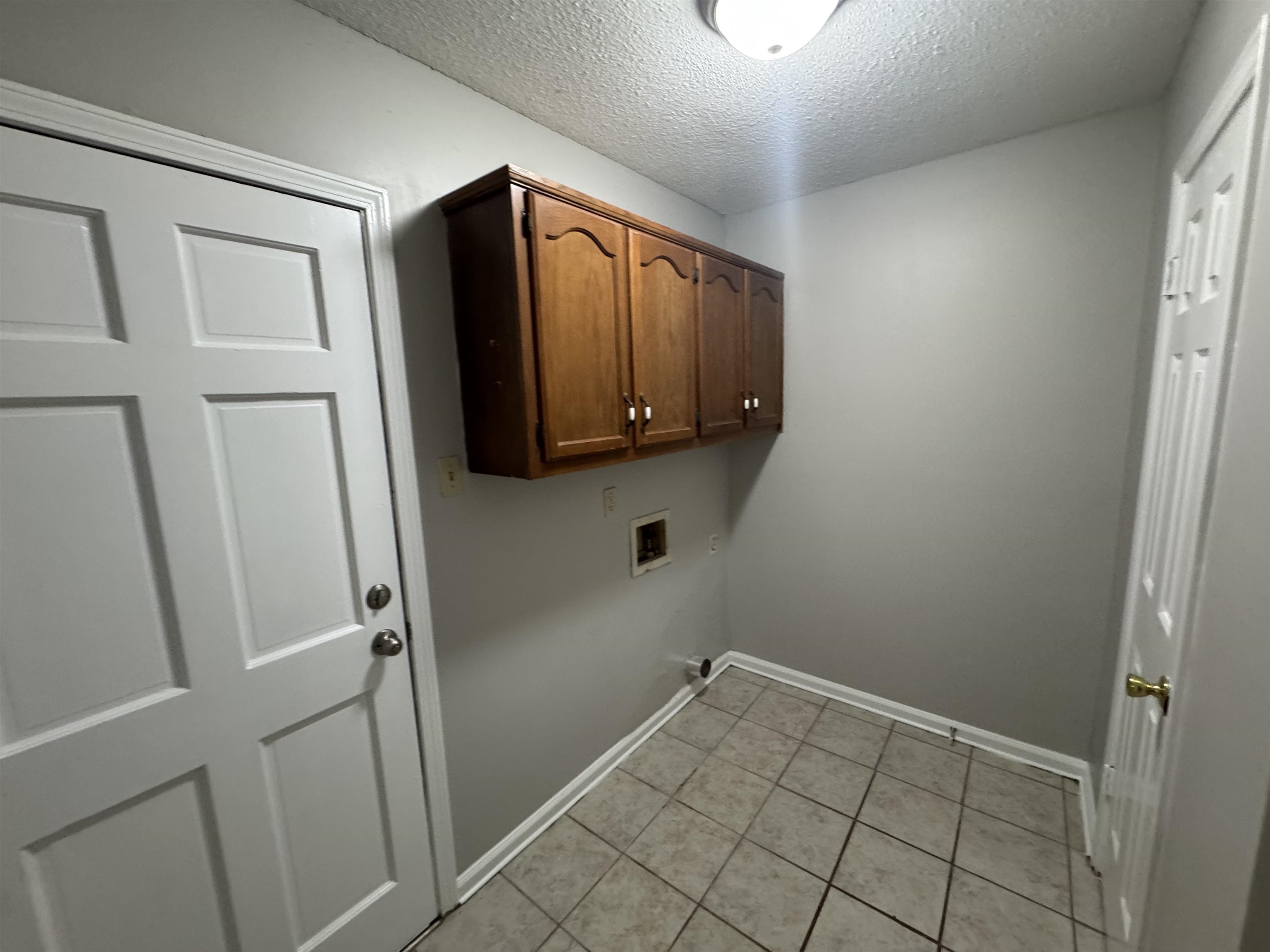 7266 Woodshire Road Memphis, TN 38125 - Photo 4 of 14 Laundry room featuring cabinet space, a textured ceiling, light tile patterned flooring, and hookup for a washing machine