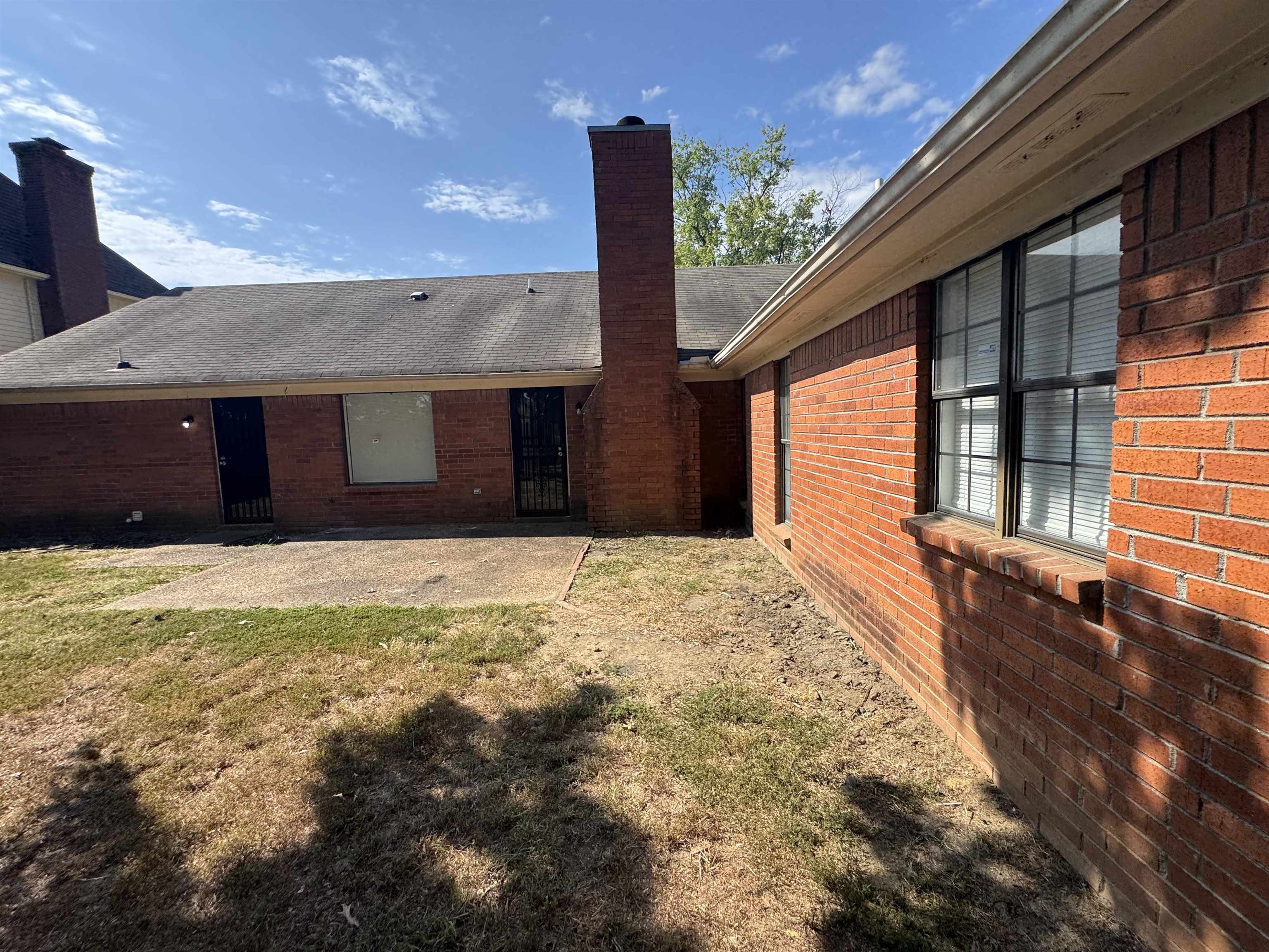 7266 Woodshire Road Memphis, TN 38125 - Photo 6 of 14 Rear view of property featuring a patio area, brick siding, a chimney, a shingled roof, and a lawn