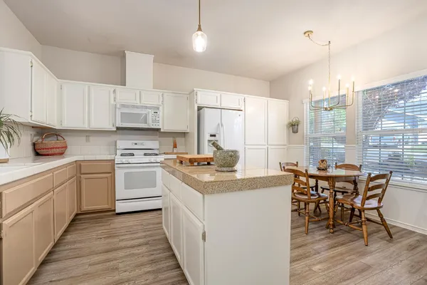 a kitchen with stainless steel appliances granite countertop a stove a sink dishwasher a refrigerator and white cabinets with wooden floor