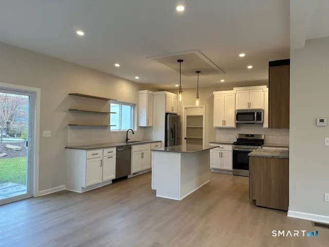 a kitchen with stainless steel appliances kitchen island granite countertop a stove top oven a sink a refrigerator and white cabinets with wooden floor