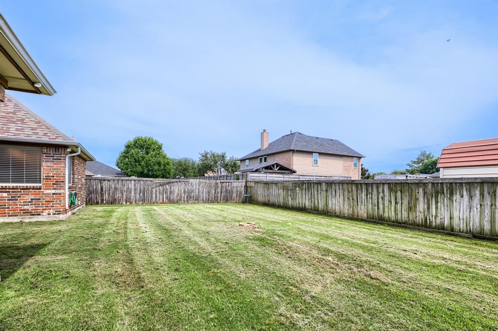 603 Ash Street Pilot Point, TX 76258 - Photo 28 of 28 Expansive backyard featuring a manicured lawn, full privacy fencing, and a red brick exterior on the property structure