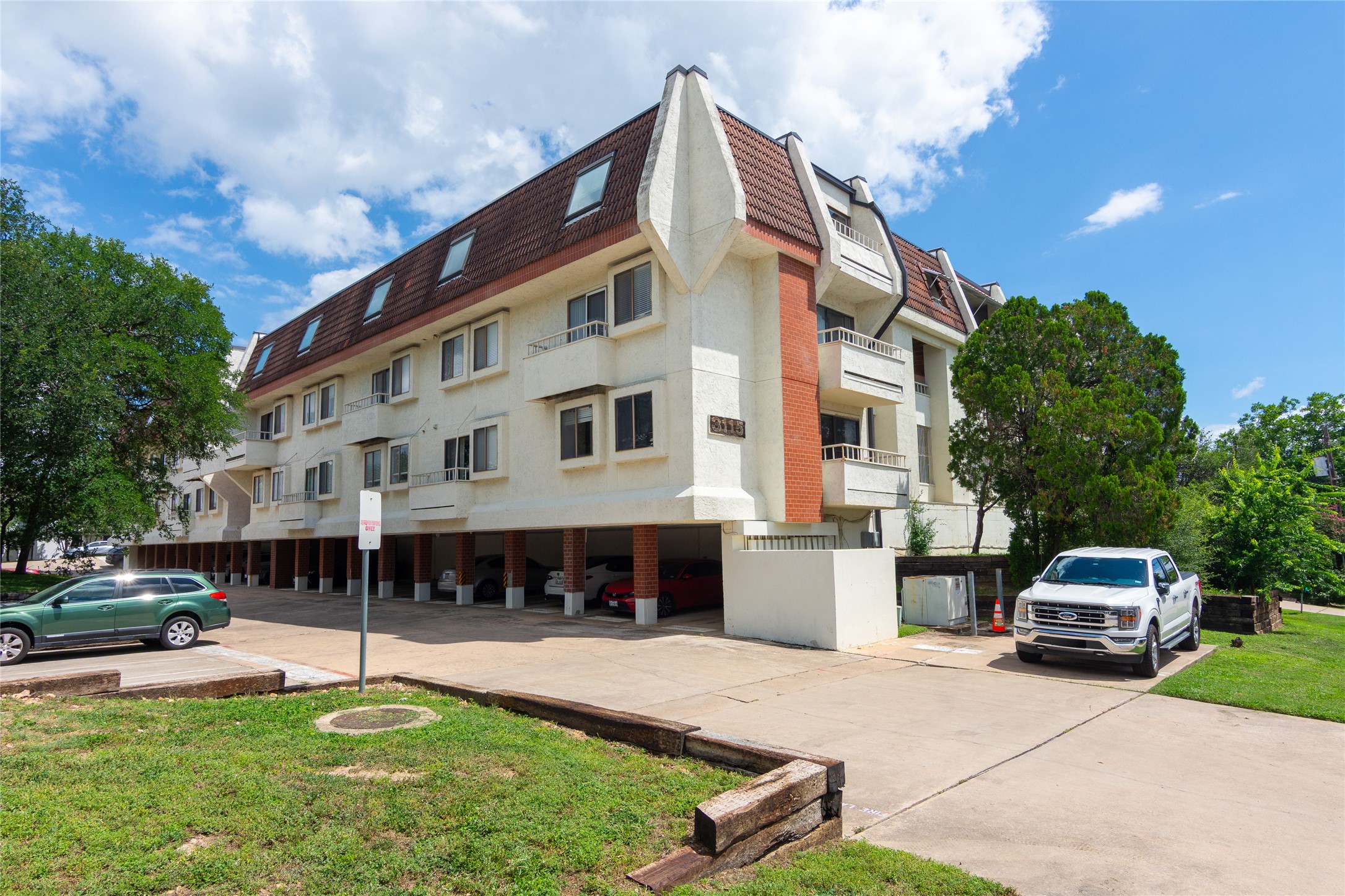 3115 Helms Street, Unit 106 Austin, TX 78705 - Photo 1 of 7 Multi-level residential building with ample covered parking, nestled amongst mature greenery.