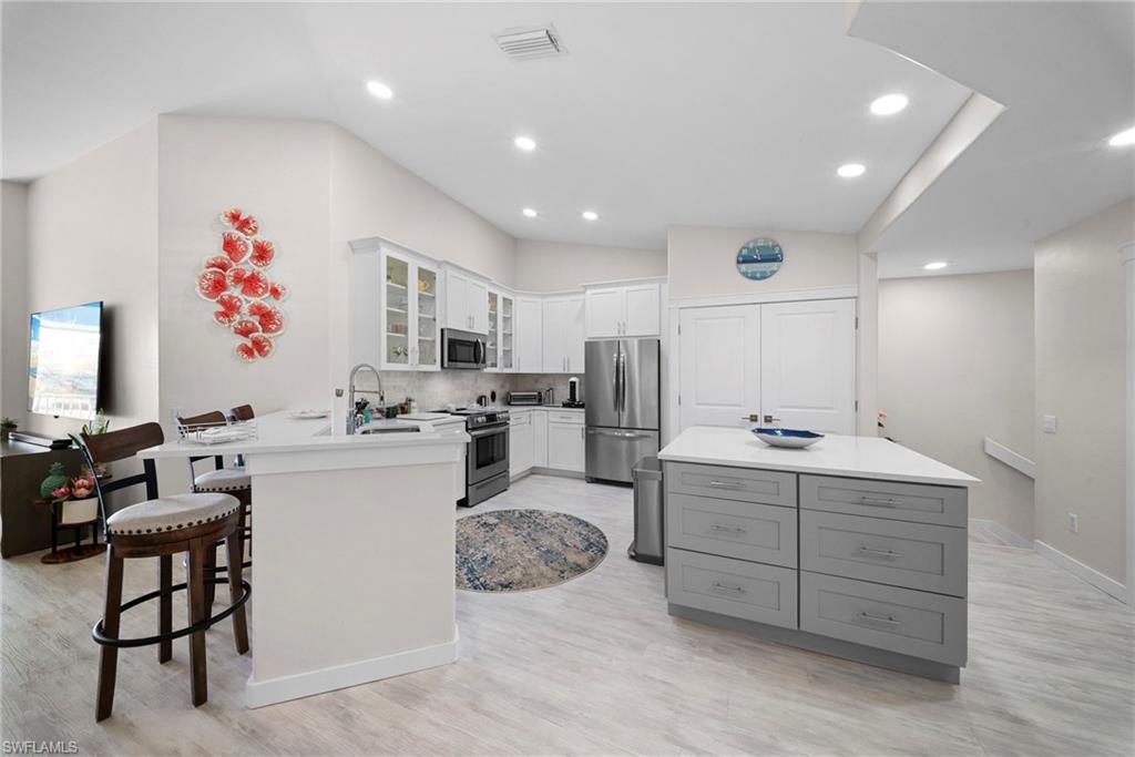 9231 Spring Run Boulevard, Unit 2109 Estero, FL 34135 - Photo 7 of 35 Kitchen with glass insert cabinets, a breakfast bar, stainless steel appliances, vaulted ceiling, and decorative backsplash