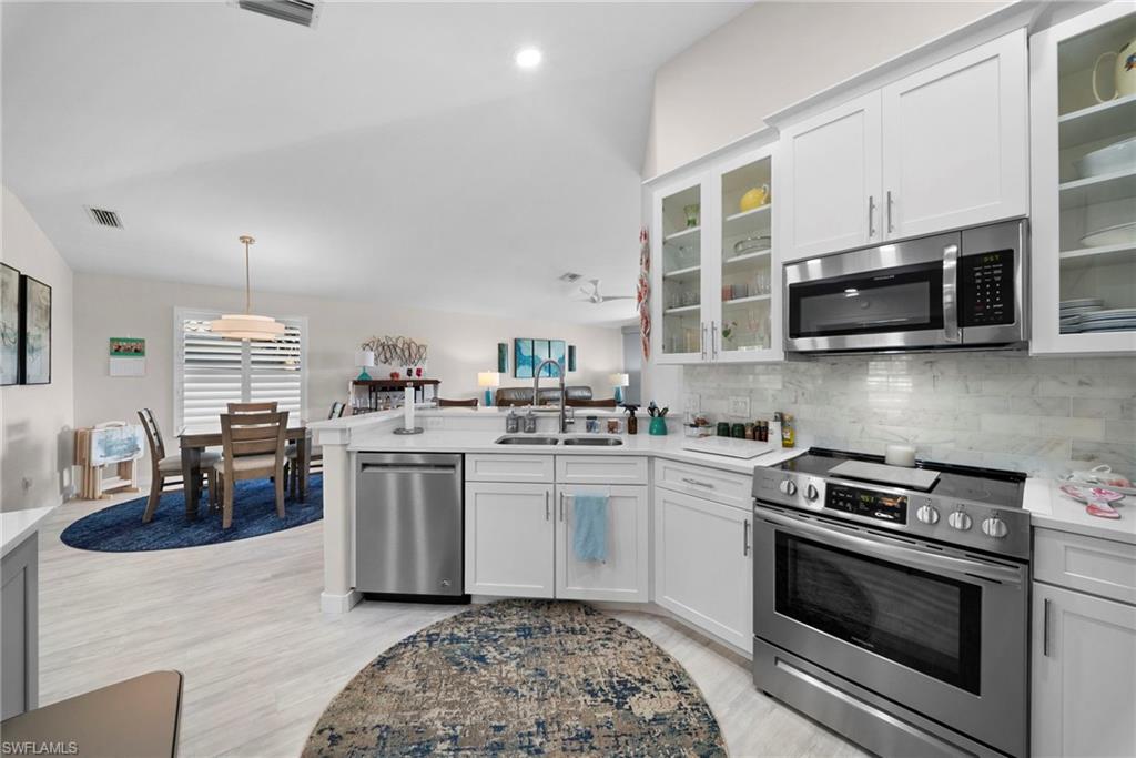 9231 Spring Run Boulevard, Unit 2109 Estero, FL 34135 - Photo 9 of 35 Kitchen featuring stainless steel appliances, a peninsula, white cabinetry, decorative backsplash, and glass insert cabinets