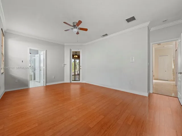 a view of an empty room with wooden floor and a ceiling fan