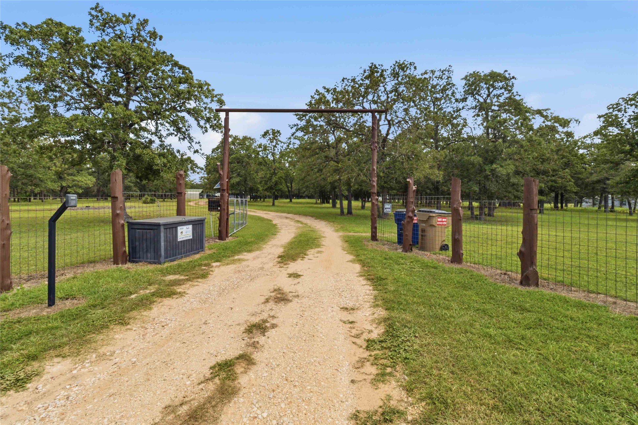 7921 Vista Ranch Road Smithville, TX 78957 - Photo 33 of 39 A private gated entry opens to a winding gravel driveway, nestled amongst mature trees and green fields.