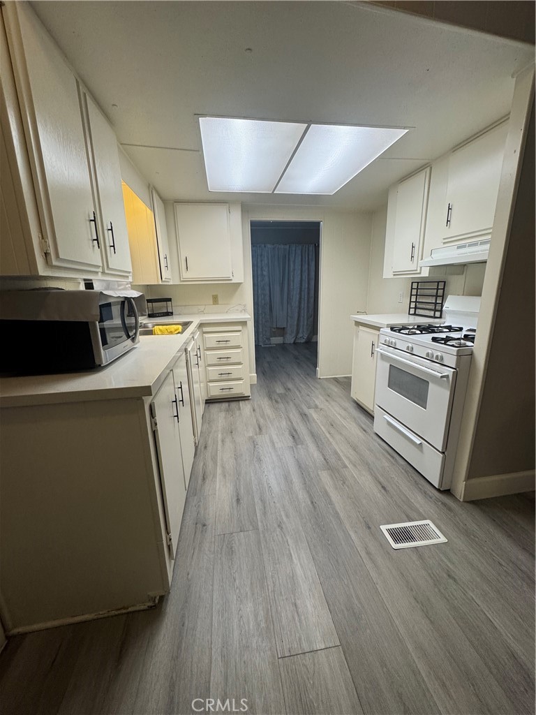 2751 Reche Canyon Road, Unit 185 Moreno Valley, CA 92555 - Photo 10 of 17 a kitchen with a wooden floor a sink a stove and cabinets