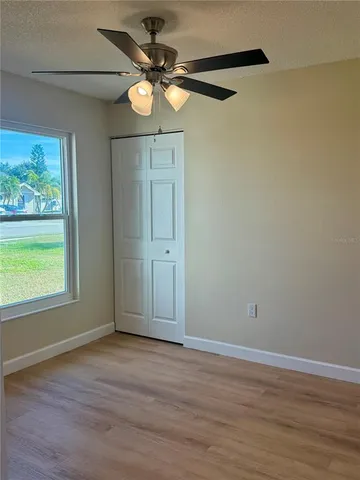 an empty room with wooden floor fan and windows