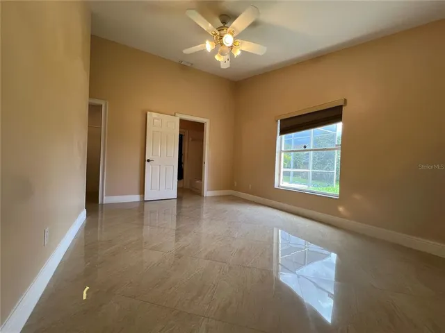 an empty room with chandelier fan and windows