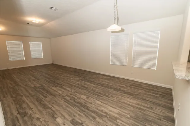 an empty room with wooden floor chandelier fan and windows