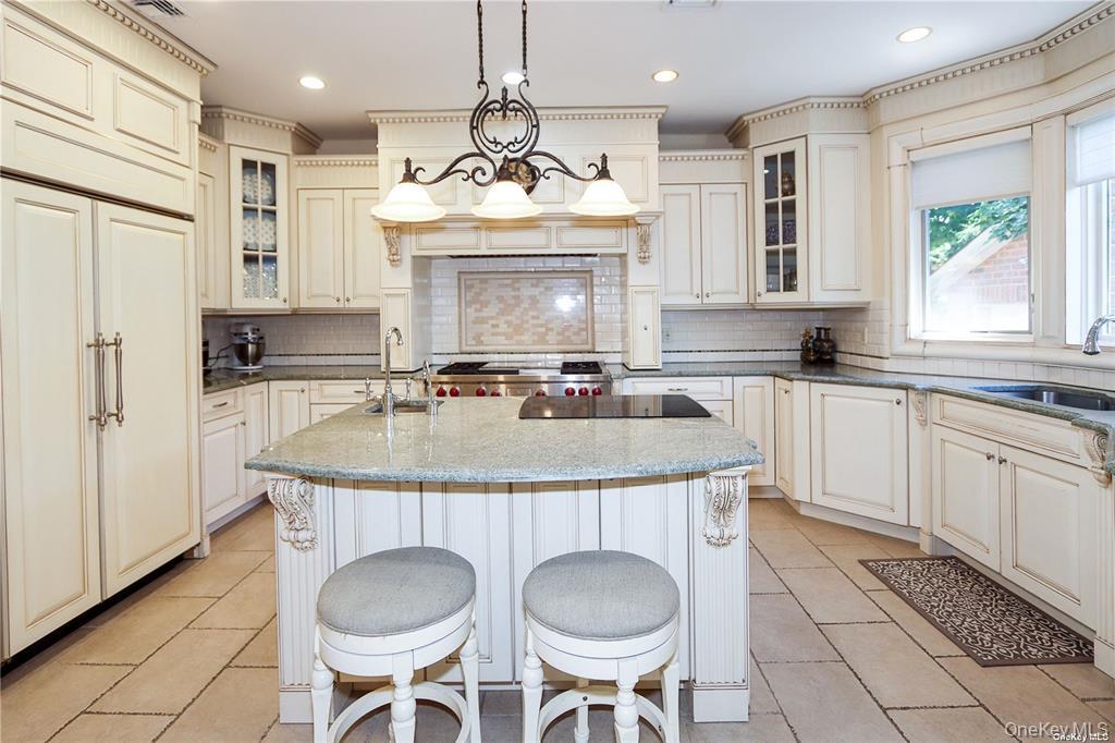 24 Steamboat Road Great Neck, NY 11024 - Photo 10 of 28 Kitchen featuring glass insert cabinets, a center island with sink, dark stone counters, hanging light fixtures, and decorative backsplash