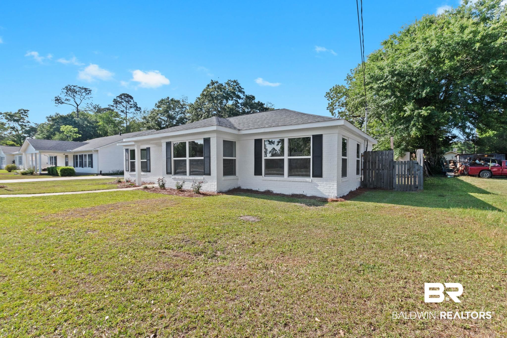 311 Cloverdale Road Atmore, AL 36502 - Photo 61 of 63 White brick exterior featuring dark window shutters, a dark shingle roof, and established landscaping