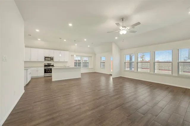a view of an empty room with wooden floor and a kitchen