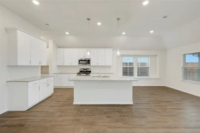 a large kitchen with stainless steel appliances granite countertop a stove top oven a sink dishwasher a microwave oven and a granite countertops with wooden floor