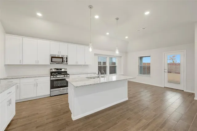 a large kitchen with kitchen island a stove a sink a refrigerator and white cabinets with wooden floor