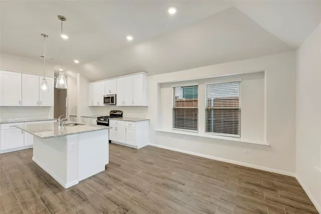 a kitchen with stainless steel appliances granite countertop a stove top oven a sink a refrigerator and white cabinets with wooden floor