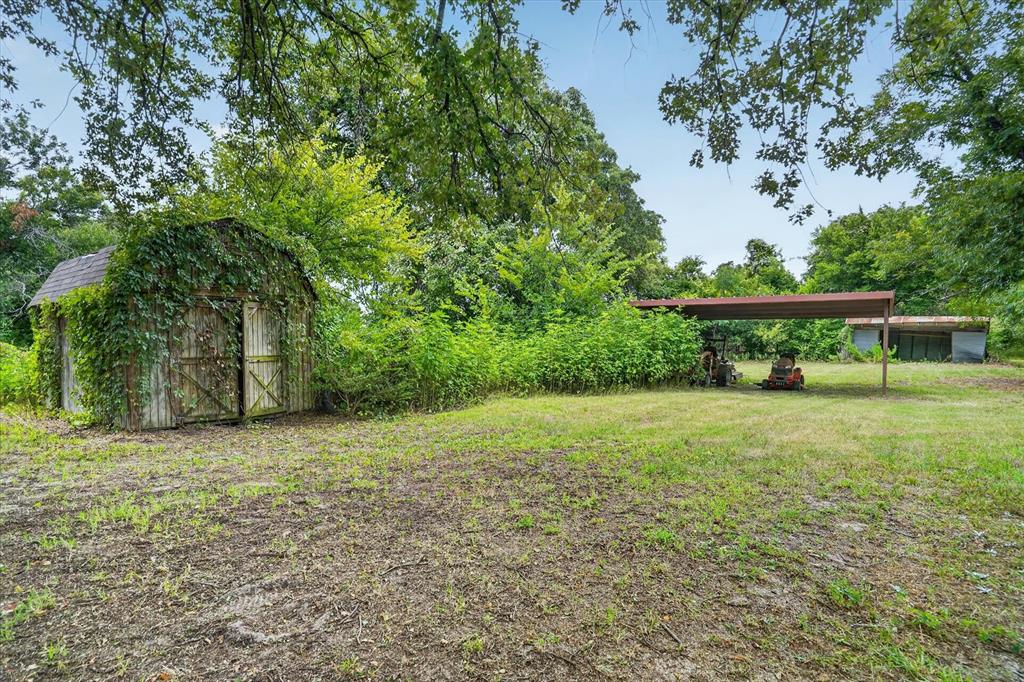 1654 Ranger Highway Weatherford, TX 76088 - Photo 28 of 31 Expansive outdoor space featuring a rustic wood shed with vine coverage, a metal-roofed carport, and mature trees providing natural shade