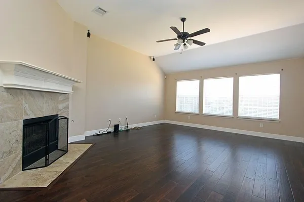 an empty room with wooden floor fireplace and windows