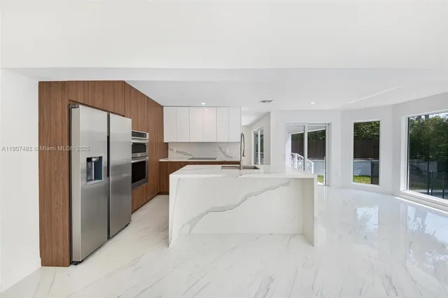a large white kitchen with kitchen island a large window and refrigerator