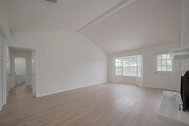 an empty room with wooden floor fireplace and windows