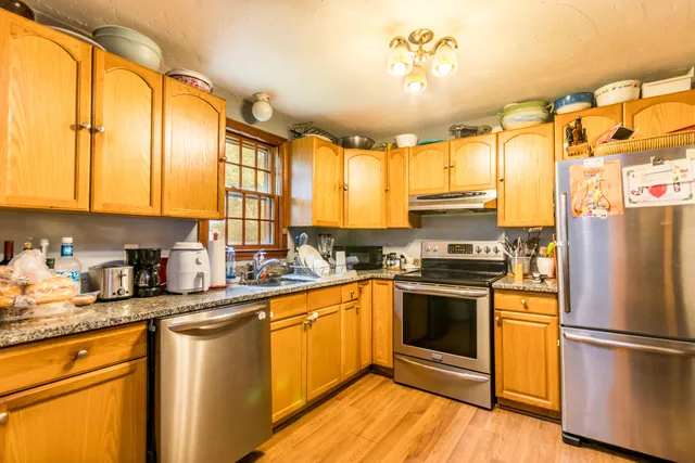 a kitchen with stainless steel appliances granite countertop a refrigerator a sink dishwasher a stove and white countertops with wooden floor