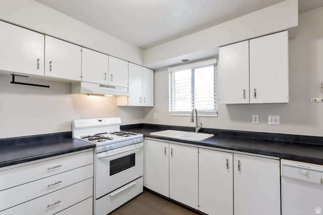 88 West 50 South, Unit J10 Centerville, UT 84014 - Photo 6 of 19 Kitchen featuring white cabinetry, dark countertops, a double basin sink, a gas range with an overhead vent, and a built-in dishwasher