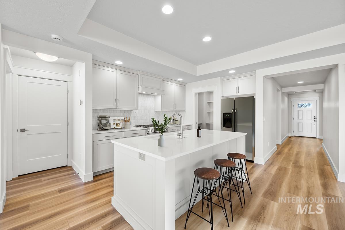 6983 South Skybreak Lane Meridian, ID 83642 - Photo 2 of 25 Kitchen with white cabinets, stainless steel appliances, a raised ceiling, a kitchen bar, and light wood-style floors