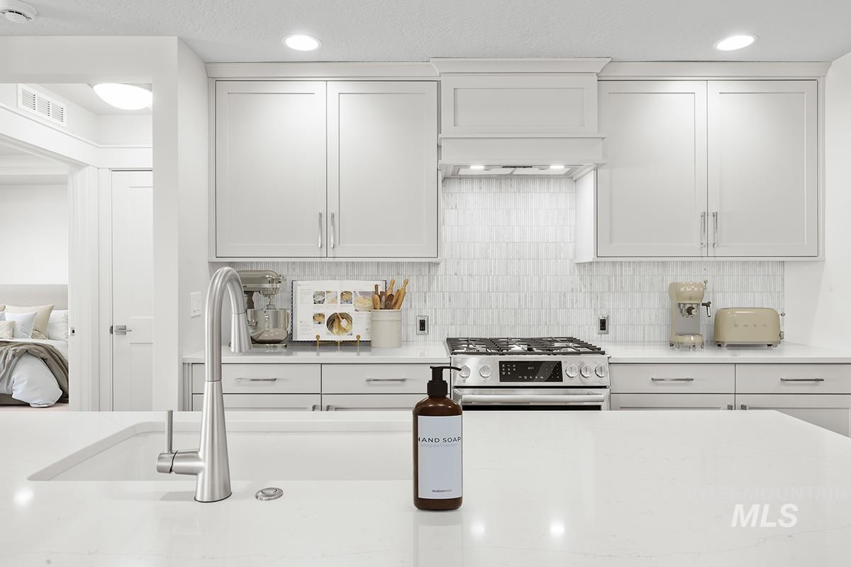 6983 South Skybreak Lane Meridian, ID 83642 - Photo 3 of 25 Kitchen with white cabinetry, stainless steel range with gas cooktop, light stone counters, decorative backsplash, and recessed lighting