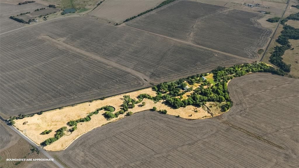 Extensive agricultural fields with bordering natural areas featuring mature trees and open land