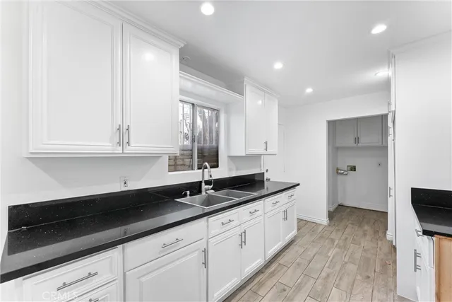 a kitchen with granite countertop white cabinets sink and a wooden floor