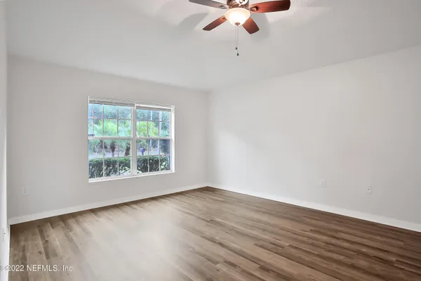 an empty room with wooden floor chandelier fan and windows