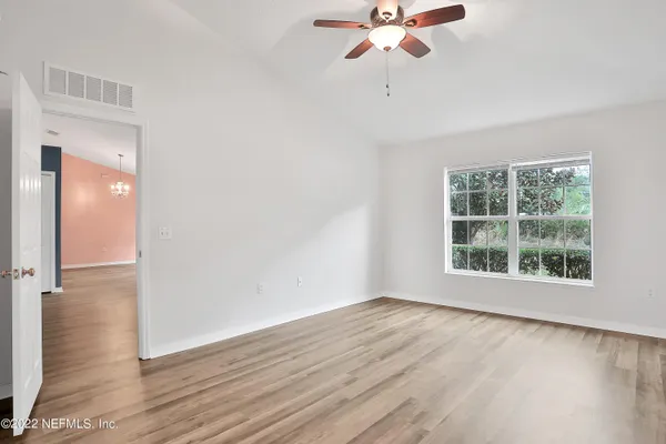 an empty room with wooden floor fan and windows