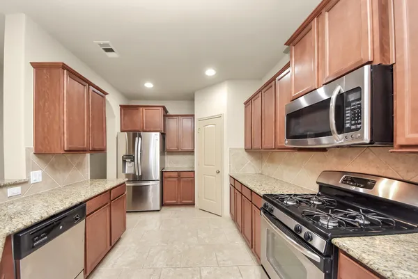 a kitchen with stainless steel appliances granite countertop a stove top oven a sink dishwasher and a refrigerator with wooden cabinets