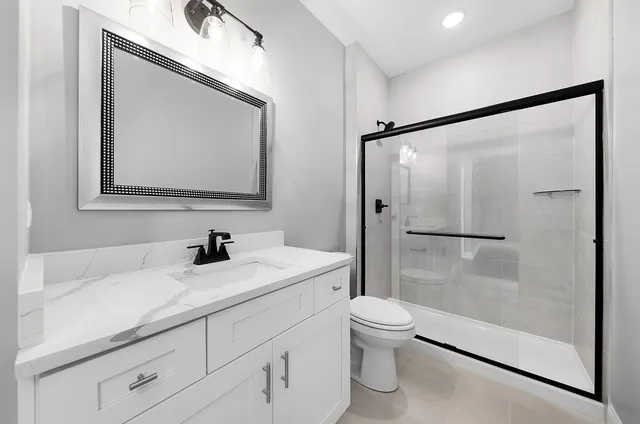 a bathroom with a granite countertop sink a toilet a mirror and shower