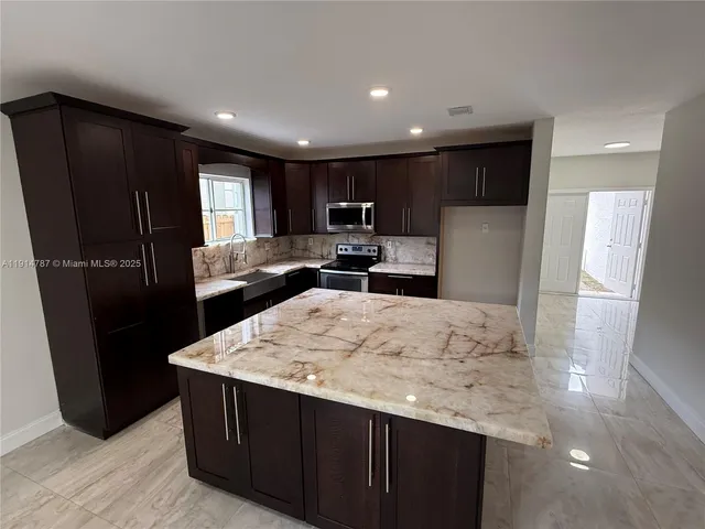 a kitchen with stainless steel appliances kitchen island granite countertop a refrigerator a sink a stove and wooden cabinets