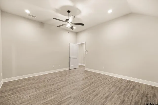 an empty room with wooden floor fan and windows