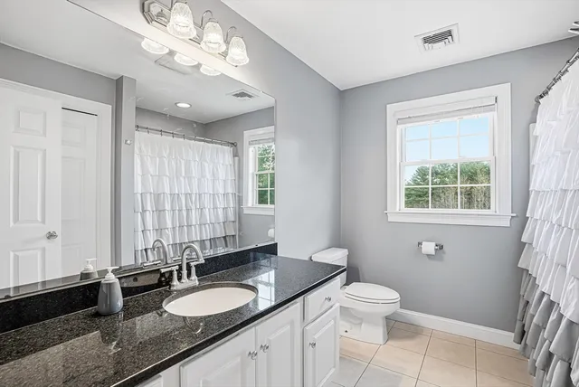 a bathroom with a granite countertop double vanity sink a mirror and a toilet