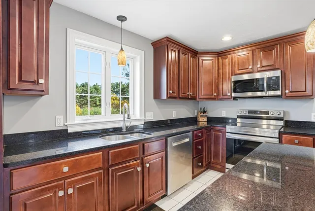 a kitchen with stainless steel appliances granite countertop a sink a stove a microwave cabinets and a window