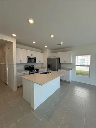 a large white kitchen with stainless steel appliances kitchen island granite countertop a large counter top a refrigerator and a stove top oven