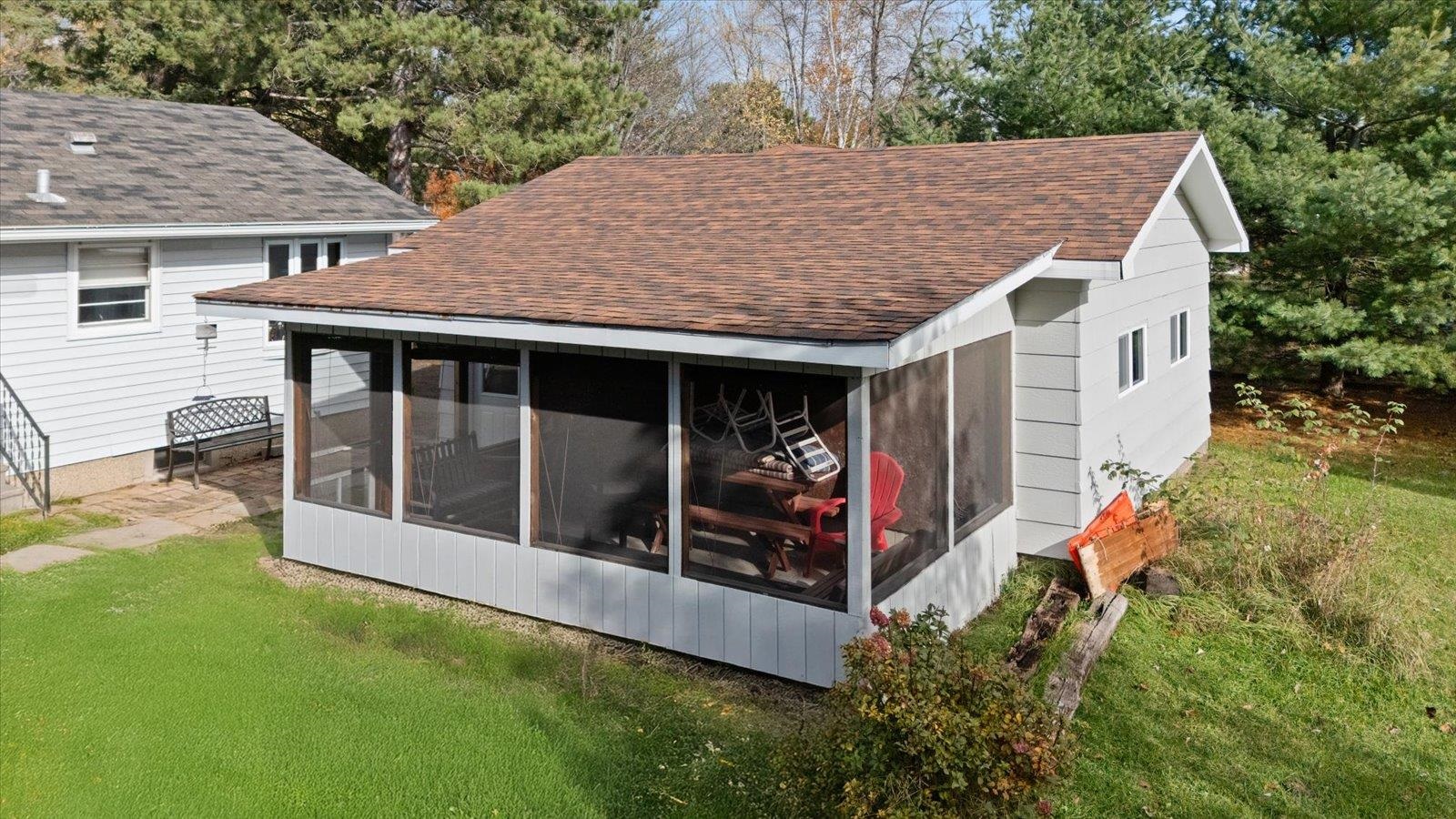 36 East Beacon Hill Road Ely, MN 55731 - Photo 3 of 30 View of home's exterior with a shingled roof, a lawn, view of wooded area, and a sunroom