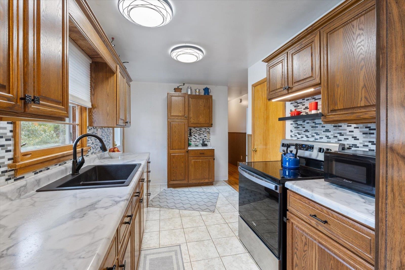 36 East Beacon Hill Road Ely, MN 55731 - Photo 5 of 30 Kitchen with decorative backsplash, stainless steel electric range, brown cabinetry, black microwave, and light tile patterned flooring
