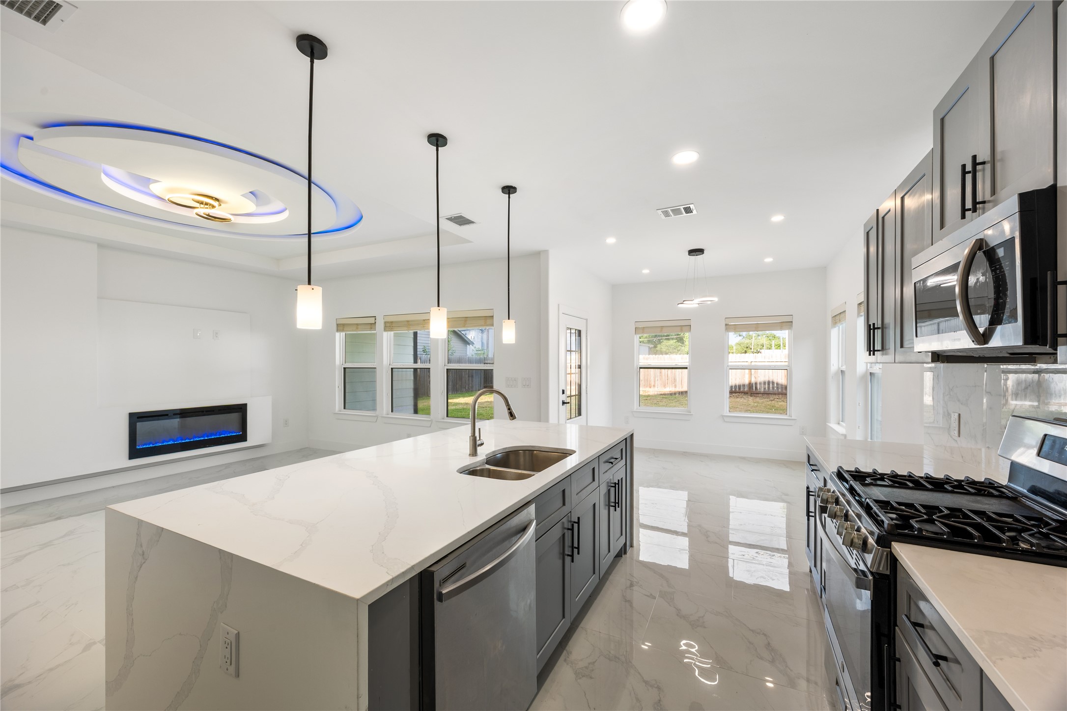 1121 Austin Street Rosenberg, TX 77471 - Photo 20 of 44 This modern kitchen features sleek cabinetry, stainless steel appliances, and a large island with a quartz countertop. The open concept flows into the living area, which includes a stylish electric fireplace and large windows for natural light. The space is well-lit with contemporary fixtures and polished tile flooring.