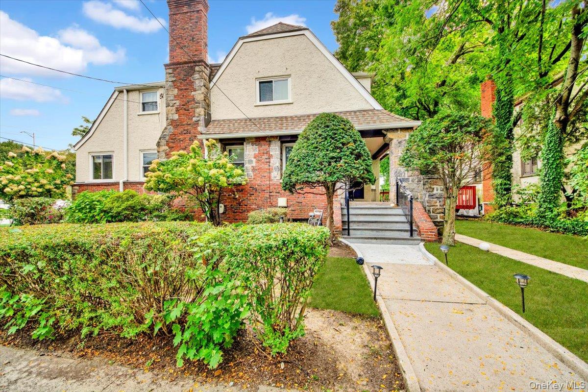 Tudor home with a front yard, brick siding, a shingled roof, a chimney, and covered porch