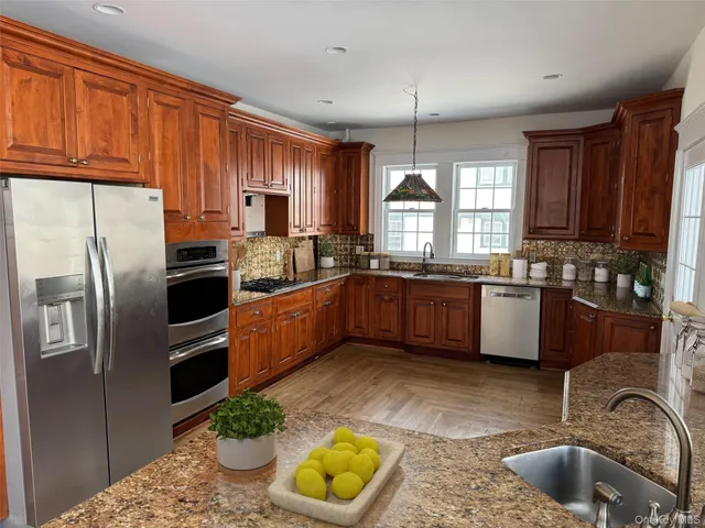 a kitchen with stainless steel appliances granite countertop a sink a stove a refrigerator cabinets and a window