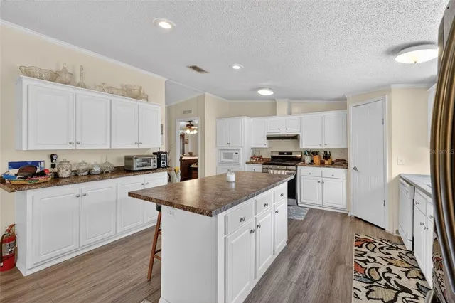 a kitchen with granite countertop a sink stove refrigerator and white cabinets with wooden floor