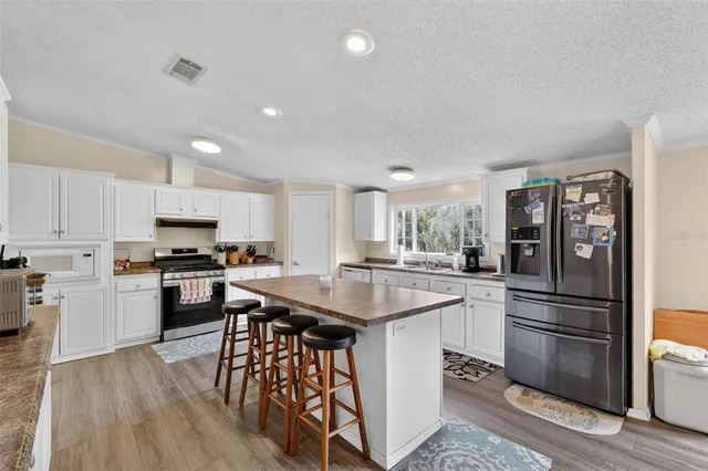 a kitchen with stainless steel appliances kitchen island granite countertop a refrigerator a stove a sink a dining table and chairs with wooden floor