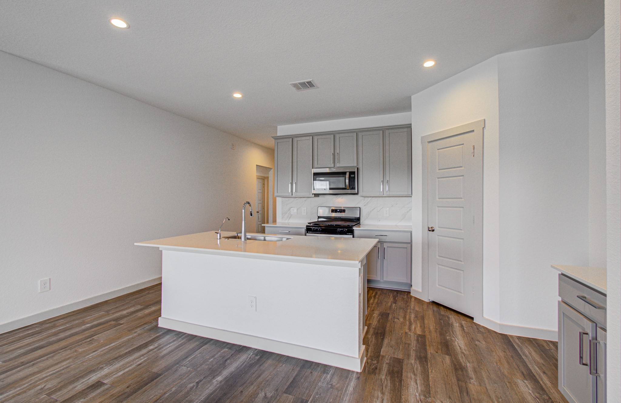7903 Wrangler Shack Lane Rosharon, TX 77583 - Photo 14 of 29 Experience the perfect blend of style and functionality in this modern kitchen, featuring sleek gray cabinets, a central island with a sink, stainless steel appliances, and warm wood-style flooring, all illuminated by bright recessed lighting.