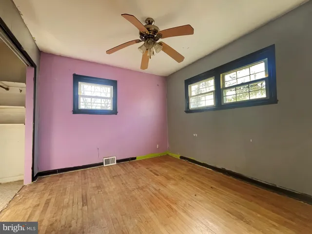 an empty room with wooden floor ceiling fan and windows