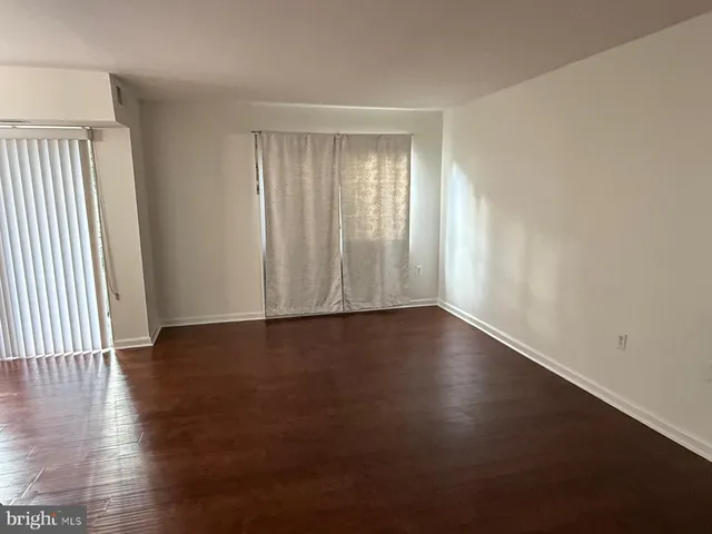 an empty room with wooden floor and windows with curtains
