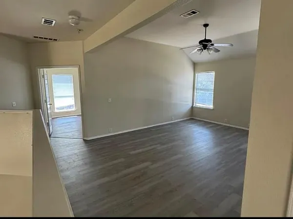 an empty room with wooden floor chandelier fan and windows